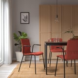 Modern dining area with red LÄKTARE chairs, dark metal frames, and wooden cabinets. Light fixture hangs over rectangular table with clear vases.