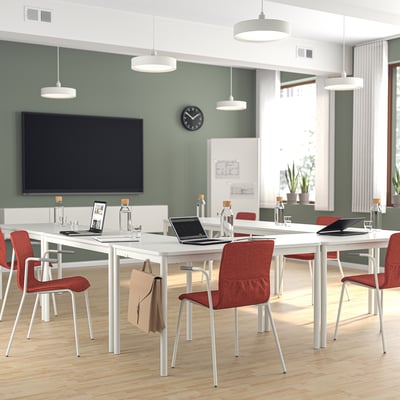 Modern office with green walls, white tables, red chairs, and a tv. Chairs are smaller than tables.