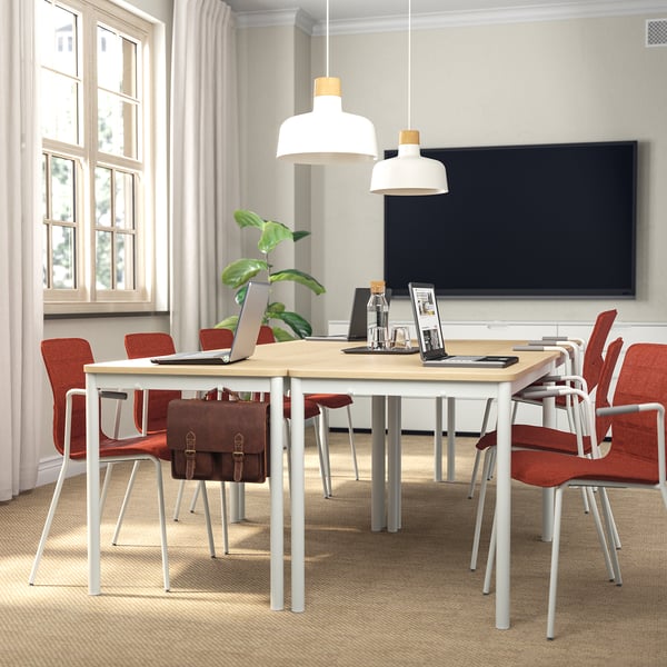 Modern conference room with wooden table, 8 red chairs, large windows, lamps, plant, laptops, blackboard, beige curtains.