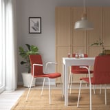 Modern dining area with red LÄKTARE chair and white frame. Wavy back and armrests, near table and cabinet, with a plant.