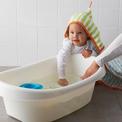Baby in bath with hooded towel, being supported by parent. Soft, white bath with non-slip bottom, and blue toy.