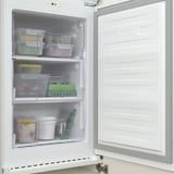 Open white integrated freezer with transparent drawers revealing food items. Positioned inside a matching cabinet.