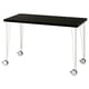 A LAGKAPTEN desk with a black tabletop and white metal legs with castors. It is rectangular and modern in design.