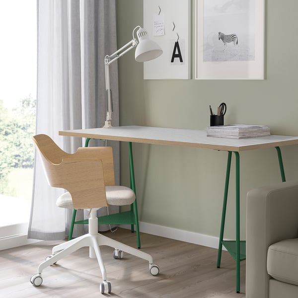 Modern home office lagkpten desk in white with green legs, wooden chair, and sleek white lamp, neatly organized with a minimalist design.