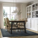 Modern dining room with blue jute rug, wooden table, chairs, pendant light, and glass cabinet.
