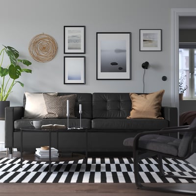 Modern living room with black sofa, rug, plant, art, and coffee table.