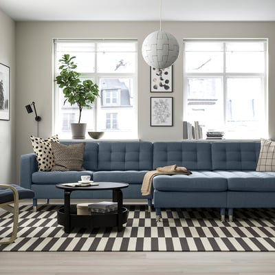 Modern living room with blue sofa, checkered rug, coffee table, pillows, plant, and white pendant light.