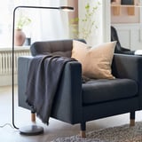 Modern grey armchair with cushions, blanket, and lamp, near window with plants