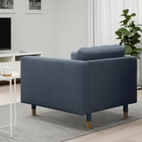 Blue armchair with wooden legs in a cozy living room, next to a cup and a green plant.