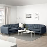 Modern living room with a blue l-shaped sofa, white coffee table, and floor lamp.