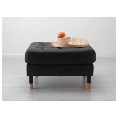 Black upholstered ottoman with wood legs, serving tray with glasses and orange.