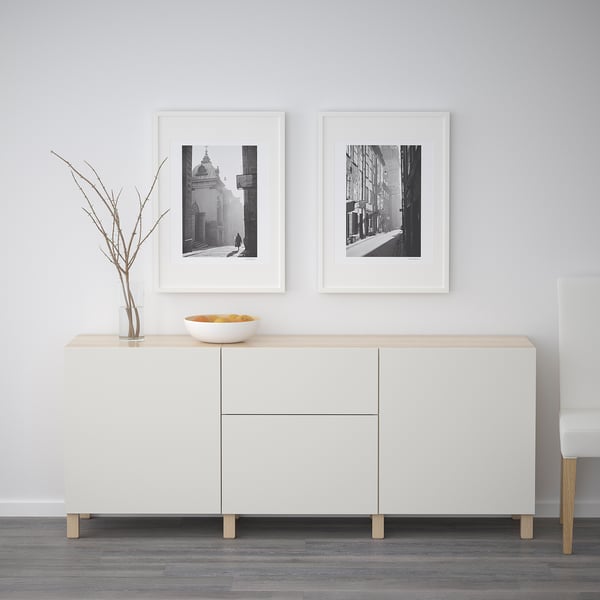 Minimalist sideboard with light wood top, displaying two black and white framed urban photos and a vase with twigs.