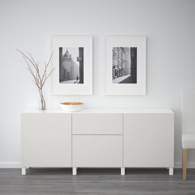 White cabinet with two drawers, sleek design, light modern look. Above are two framed black and white pictures, one bowl, and a vase with branches.