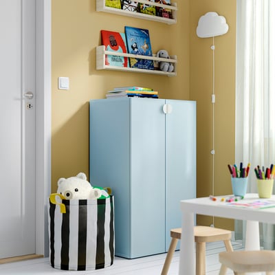 Childs room with blue LASTARE cabinet, books, teddy bear. Between door and table, taller than stool but shorter than door.