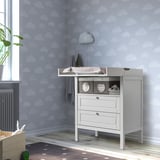 Light blue cloud nursery with white changing table, plant, and toy basket.