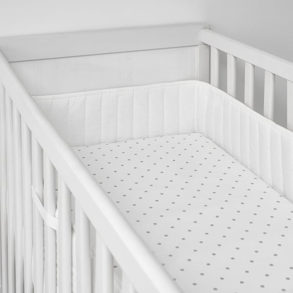 Empty white crib with polka dot sheet and padded sides.
