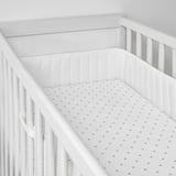 Empty white crib with polka dot sheet and padded sides.