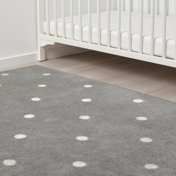 Childs room with white crib, grey rug with white dots, placed on wooden floor.