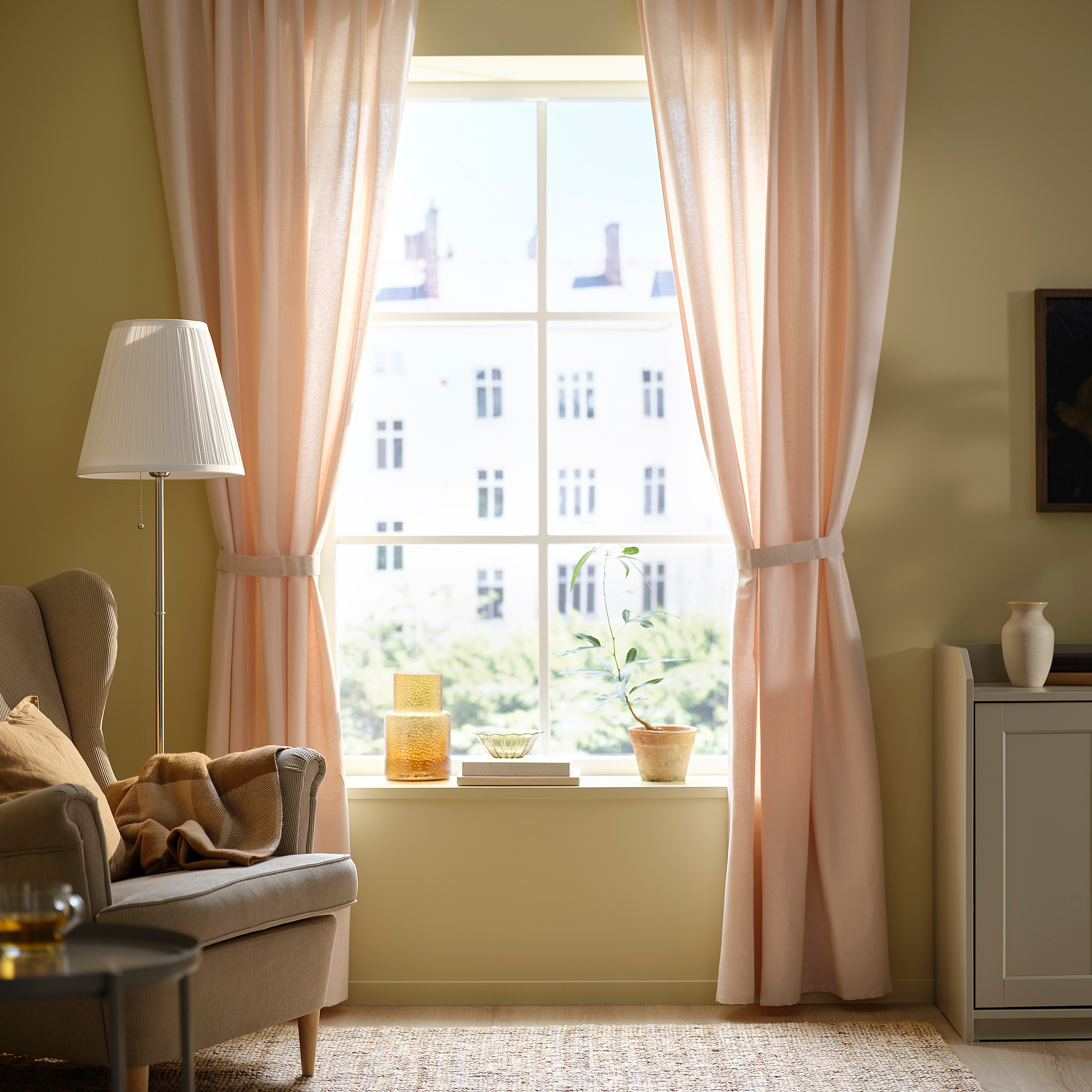Bright room with LENDA light pink curtains, armchair, lamp, side table, and plant on windowsill.