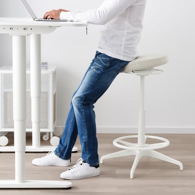 Person using LIDKULLEN sit/stand support at white desk, promoting active sitting and good posture.