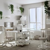 Modern white office with adjustable desks, chairs, and shelves adorned with plants and decor.