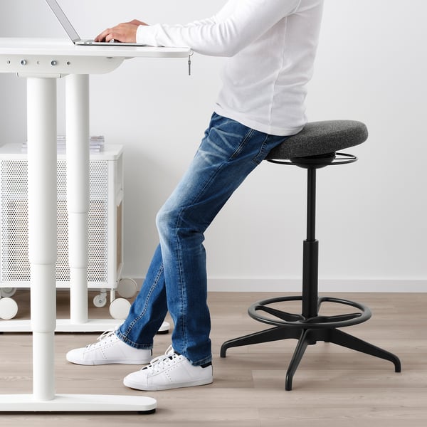Person using sit/stand support cushion at office desk, promoting active sitting and posture improvement.