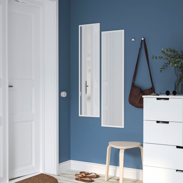 A modern blue room with a vertical LILJETRÄD mirror, white dresser, handbag, plant, stool, and sandals.
