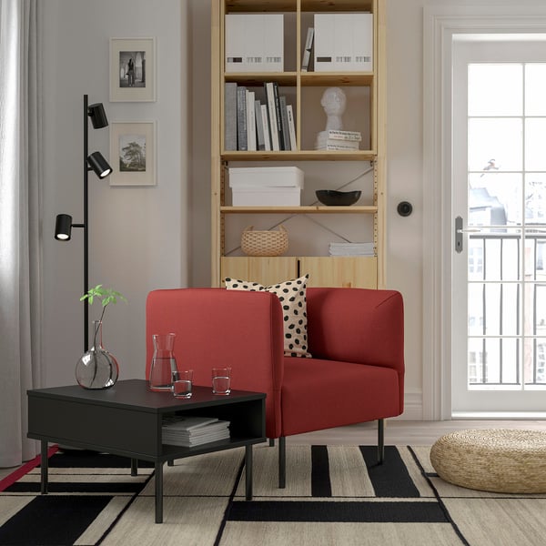 Modern living room with red sofa, bookshelf, coffee table, rug, lamp, & natural light.