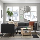 Modern living room with a large grey LILLEHEM sectional sofa, wooden coffee table, patterned rug, and large windows offering an urban view.