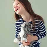 Young girl smiling, holding a plush gray toy kitten.