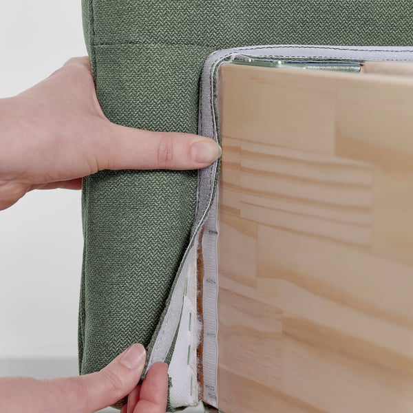 Image shows person opening grey green divan bed. LILLFJÄLLET model, sloped headboard with cushions.