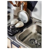 Black LILLHAVET dish rack with plates, bowls, cups, and cutlery. Stainless steel sink, wooden utensils, and white countertop.