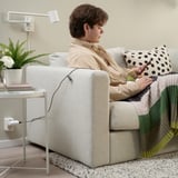 Person on couch knitting, tablet in hand, beige shirt, multicolored blanket, black dot pillow.