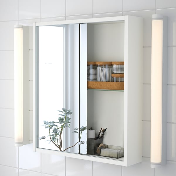Mirrored cabinet with sliding doors reveals organized toiletries and brushes. A plant with lights adds a modern touch.