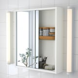 Mirrored cabinet with sliding doors reveals organized toiletries and brushes. A plant with lights adds a modern touch.