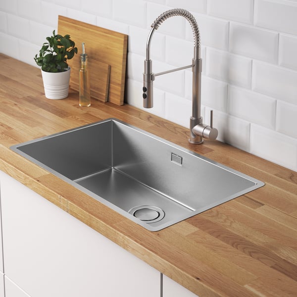 Modern kitchen sink with a brushed steel faucet, wooden countertop, and plant. A stainless steel strainer lid.