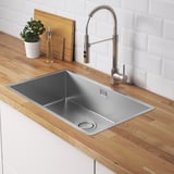 Modern kitchen sink with a brushed steel faucet, wooden countertop, and plant. A stainless steel strainer lid.