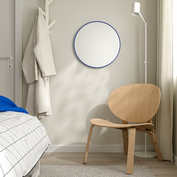 Modern bedroom with blue round mirror, light chair, checkered bed, simplicity reflected.