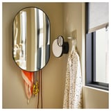 Modern black oval mirror with hooks. Displays scarves and jewelry, reflecting a room.