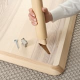 Person is assembling a wooden table. Tools and screws are on the table.