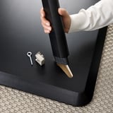 Hand inserting bolt through table hole, assembly step for LISABO table, with keyhole and connector.