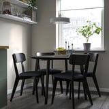 Modern dining set with black chairs and round table, positioned by a window.