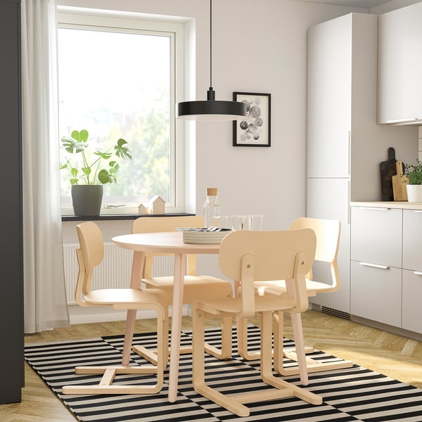 A modern dining setup with a wooden table, chairs, black pendant light, and a plant by the window.