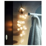 Decorative white led lights hang from a gold hook near a towel on a white rod, creating a cozy ambiance.