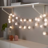 Deco string light with fluffy pom-poms on shelf. Lights up space with warm white leds.