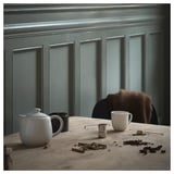 Cozy tea setup on wooden table with blue wall. Kettle, strainer, mug, tea, and cinnamon.