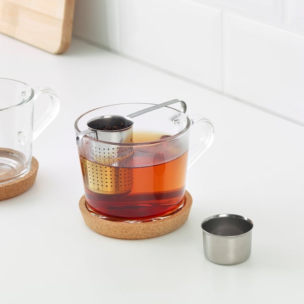 Glass mug with tea infuser; tea sits on coaster.