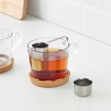 Glass mug with tea infuser; tea sits on coaster.
