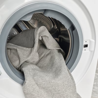A white washing machine with a gray blanket partially loaded inside.