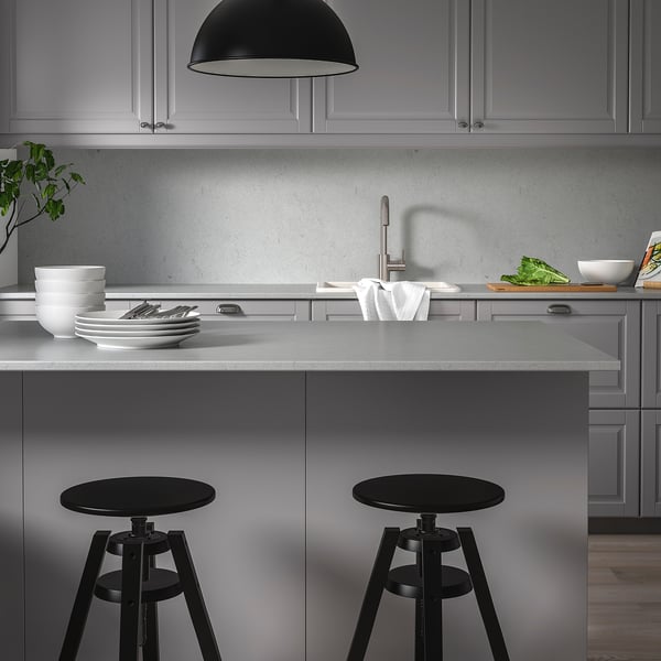 Modern kitchen with grey LOCKEBO recycled glass countertops, black round stools, sleek appliances, and minimalist design.